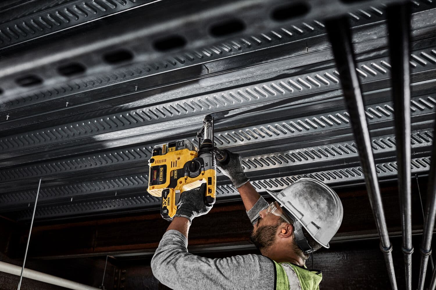 Una persona con equipo de protección utiliza un taladro rotatorio DEWALT (DCH273P2) para perforar una estructura de techo de metal en un sitio de construcción.