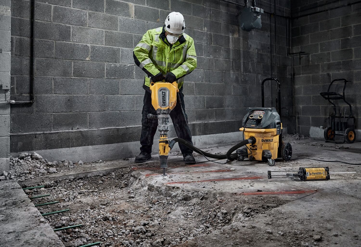 Trabajador usa martillo demoledor DEWALT para romper concreto en interior. Equipo de seguridad visible.