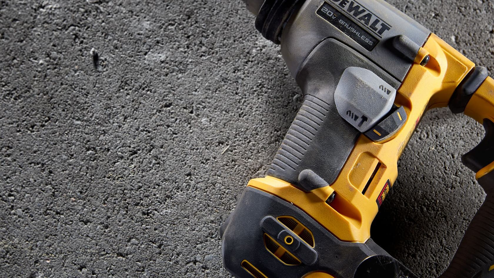 Primer plano de una herramienta eléctrica DEWALT 20V sin escobillas, parcialmente visible, colocada sobre una superficie de concreto rugoso.