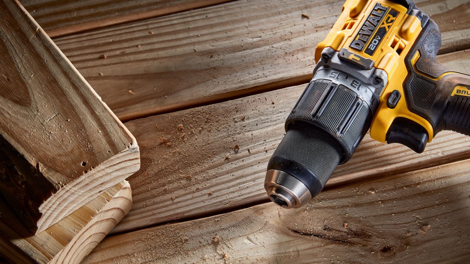 Primer plano de un taladro inalámbrico DEWALT 20V XR usado sobre una superficie de madera, con virutas de madera visibles.