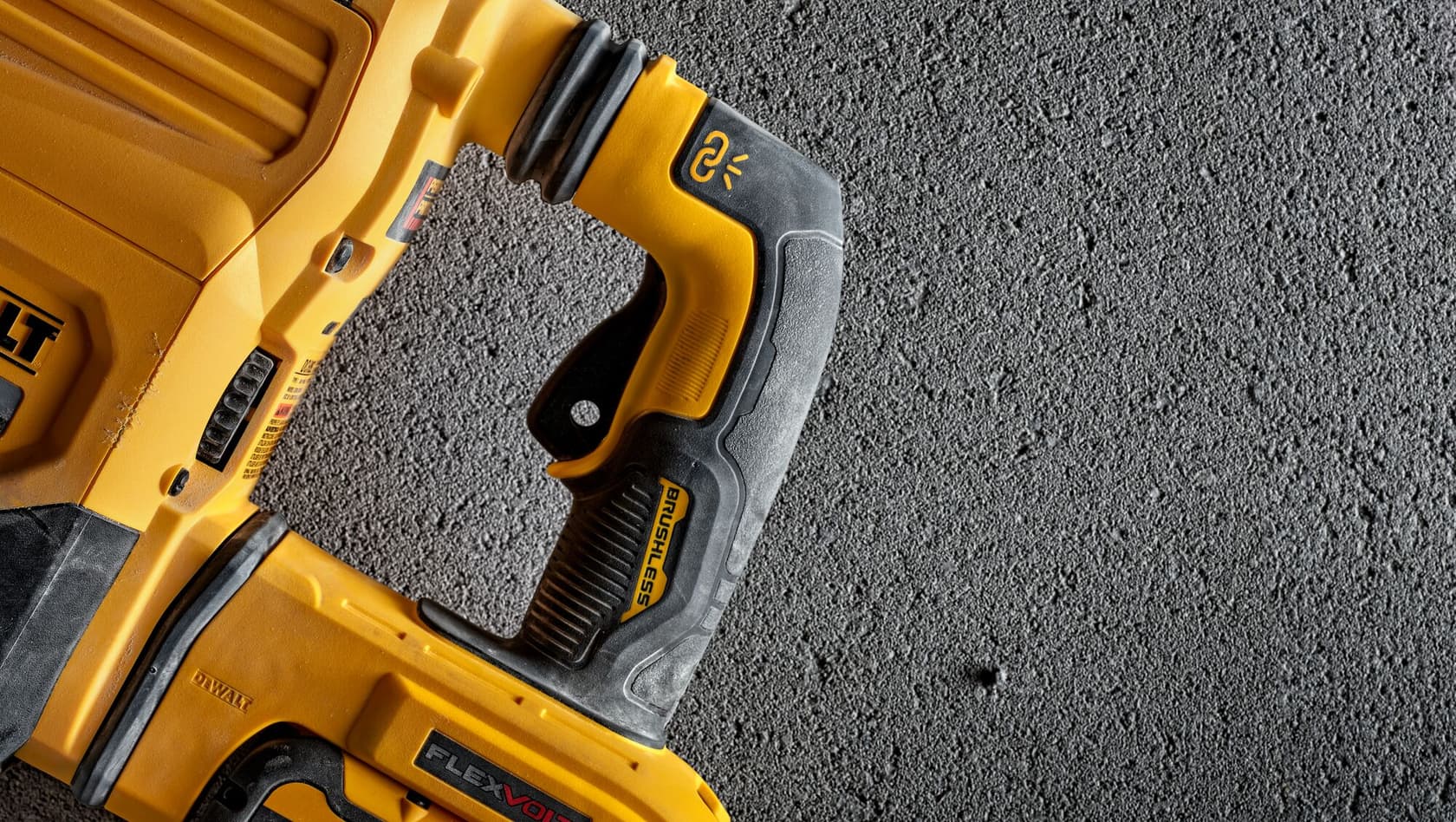 Primer plano de una herramienta eléctrica DEWALT, mostrando el mango y parte del cuerpo con la marca y los botones, colocada sobre una superficie de hormigón texturizado.