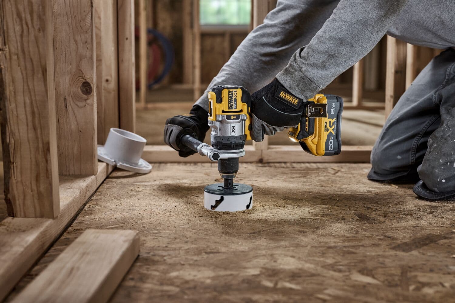 Persona usa un taladro inalámbrico DEWALT para cortar un agujero en un piso de madera en construcción.