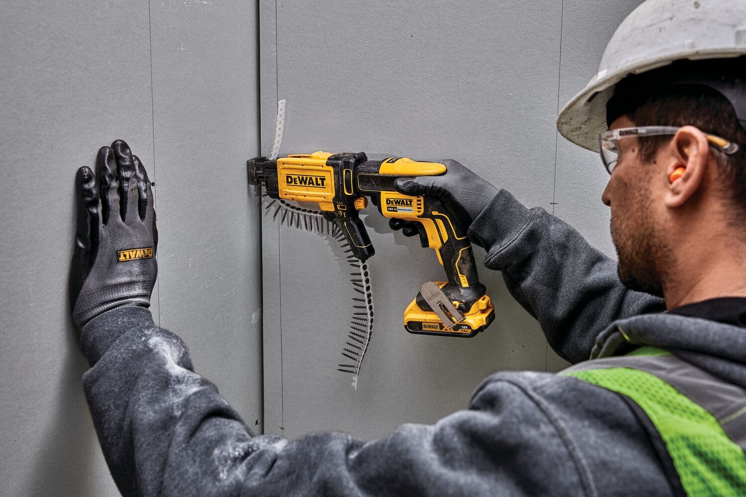 Trabajador usa la herramienta DEWALT DCF6202 para drywall, con guantes, casco y gafas protectoras.