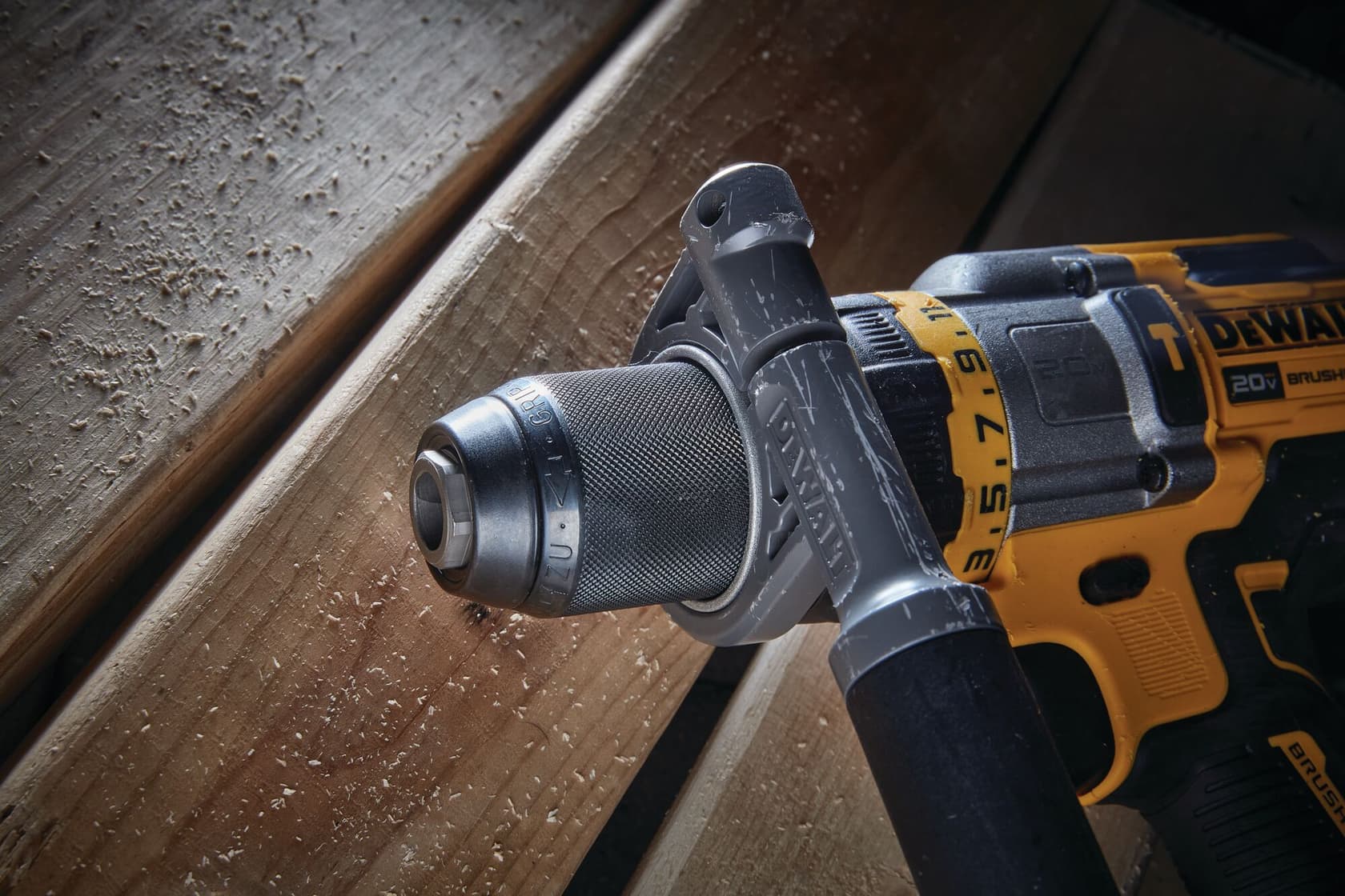 Vista en primer plano de un taladro inalámbrico DEWALT 20V brushless, modelo DCD999B, con asa lateral, apoyado sobre tablas de madera.