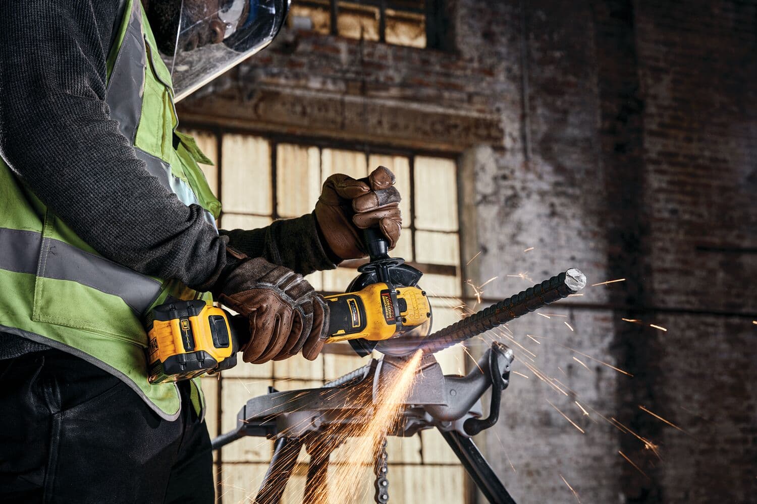 Una persona con guantes de seguridad y pantalla facial utiliza una amoladora angular inalámbrica amarilla DEWALT (modelo DCG416B) para cortar una barra de metal, produciendo chispas en un entorno industrial.