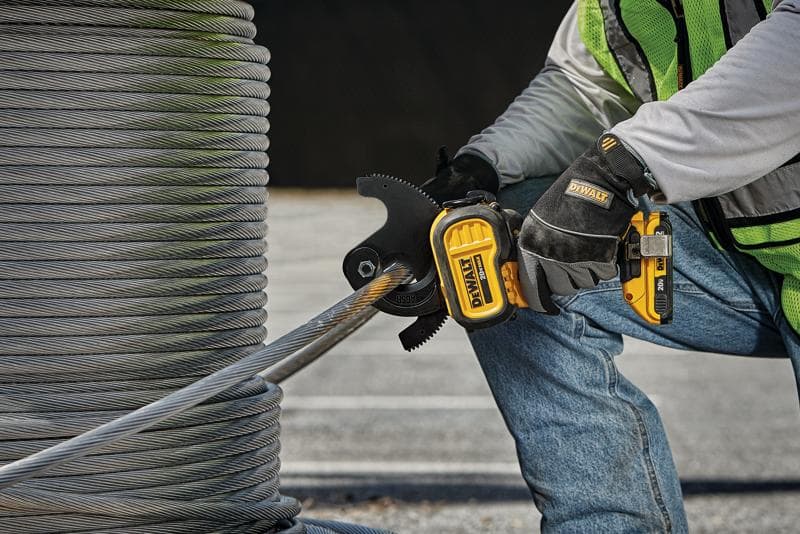 Una persona con guantes de seguridad y chaleco reflectante utiliza una herramienta eléctrica inalámbrica DEWALT para cortar un cable metálico grueso junto a una gran bobina de alambre al aire libre.