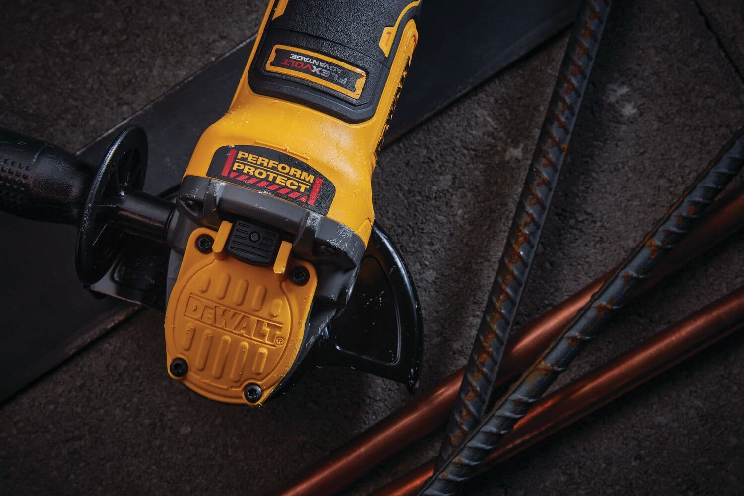Vista en primer plano de una amoladora angular inalámbrica DEWALT con mango amarillo y negro, colocada sobre una superficie oscura texturizada junto a barras metálicas.