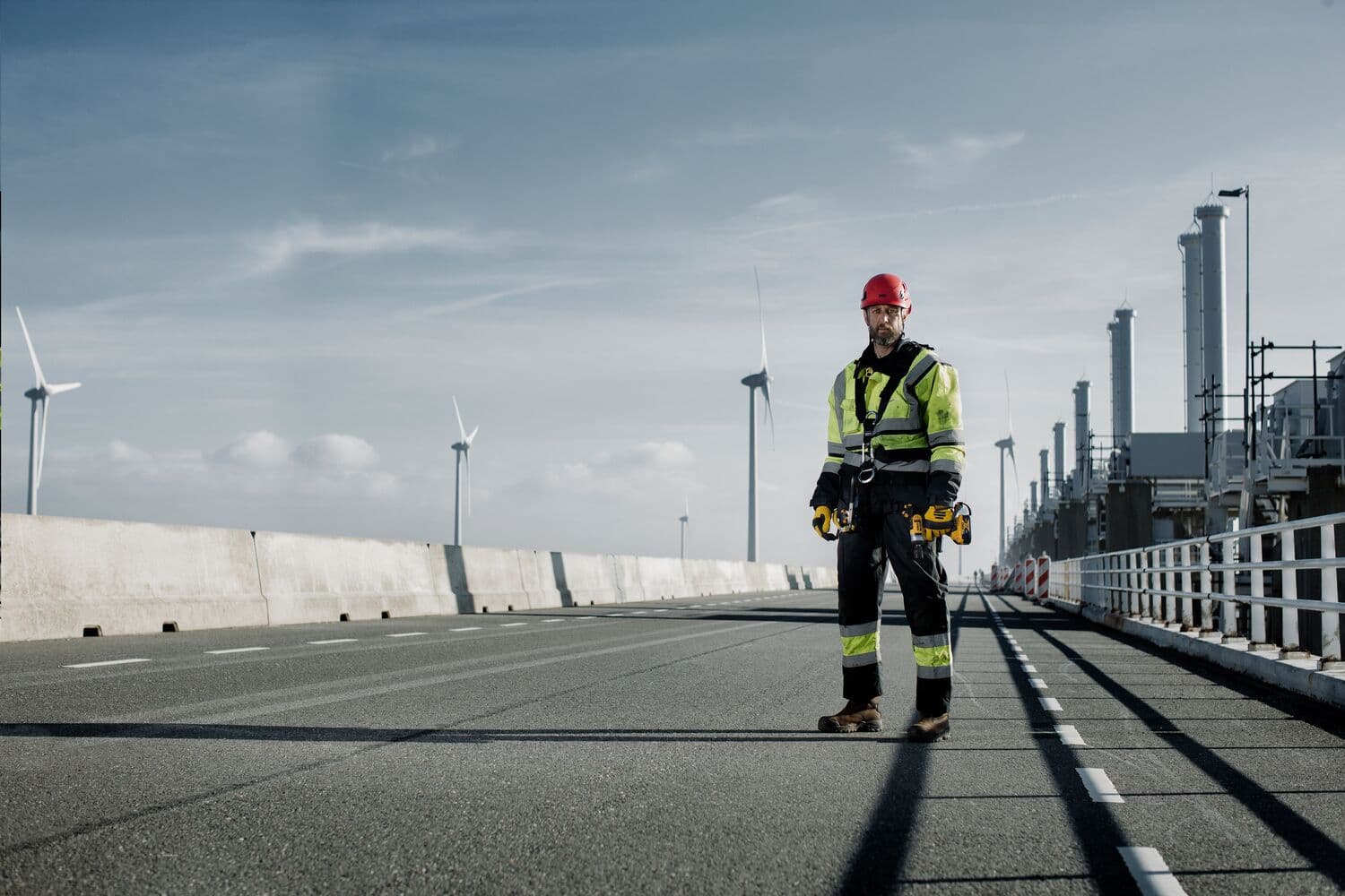Un trabajador de la construcción con chaqueta de alta visibilidad y casco rojo está en una carretera industrial sosteniendo