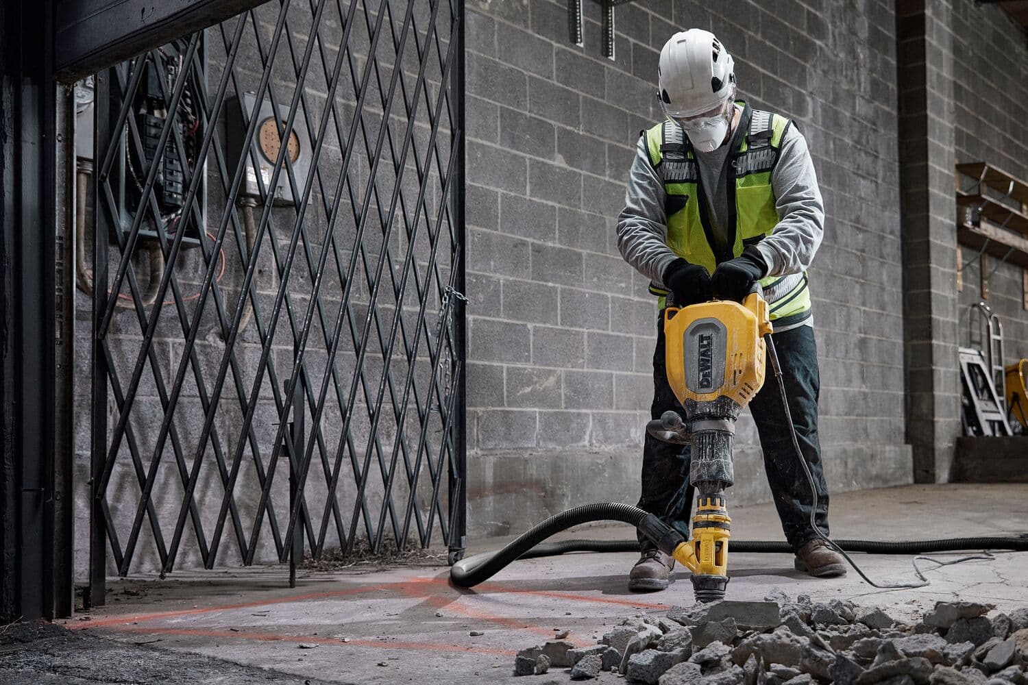 Trabajador rompe suelo de hormigón con martillo DEWALT D25911K, escombros sobre el suelo.