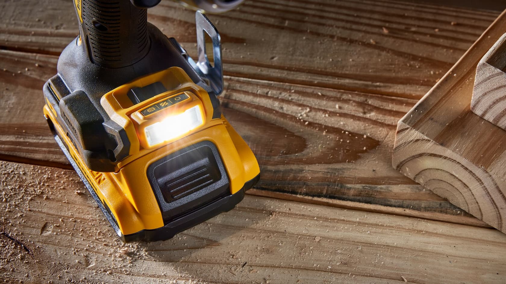 Vista de primer plano de la base de un taladro eléctrico DEWALT con una luz de trabajo LED encendida, apoyado sobre una superficie de madera con aserrín.