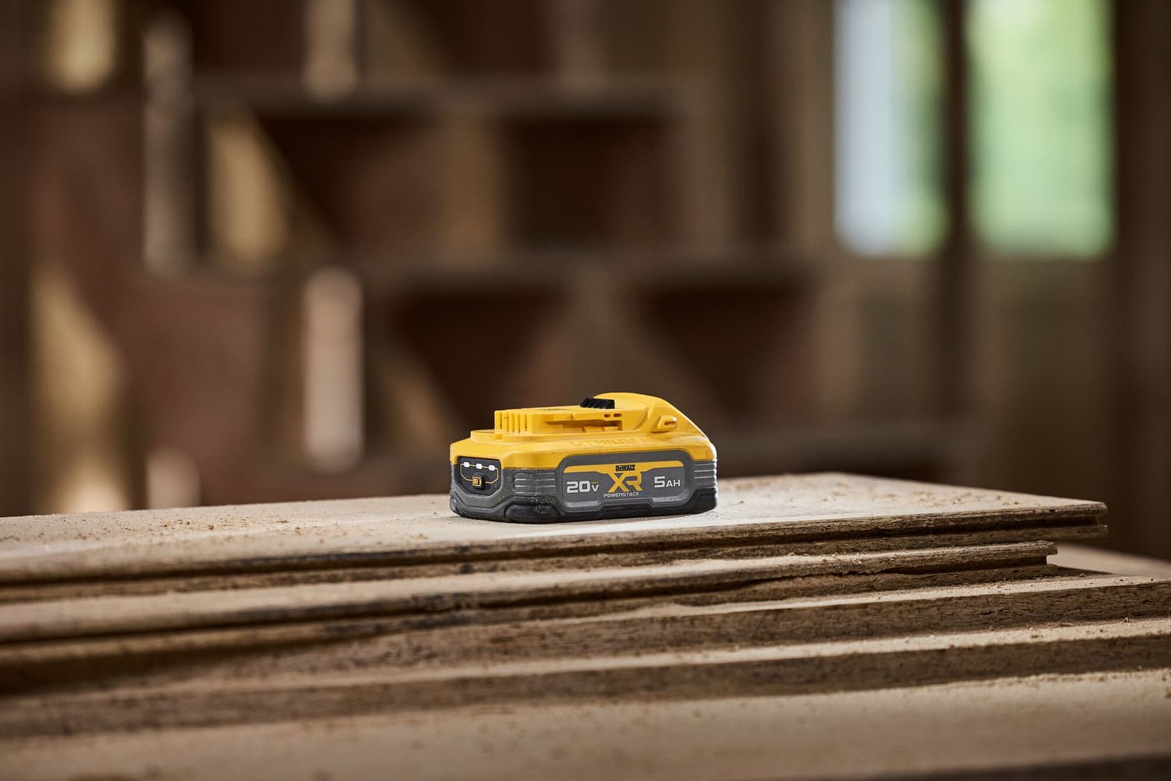 Un paquete de batería de iones de litio DEWALT 20V XR de 5,0Ah de capacidad está colocado sobre tablas de madera apiladas en un taller.