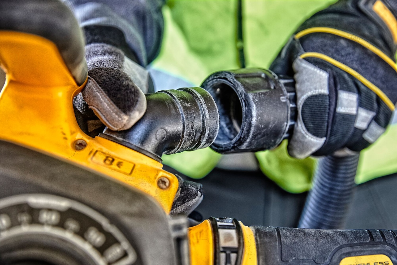 Manos enguantadas conectan una manguera a una herramienta eléctrica DEWALT amarilla.
