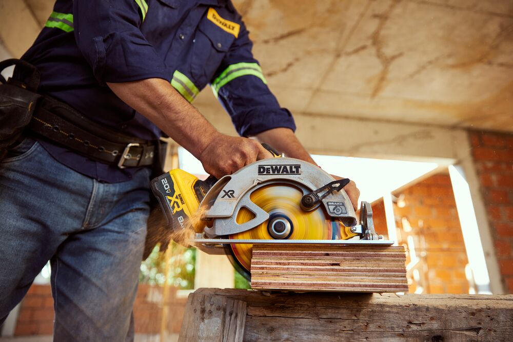 Persona usando sierra circular DEWALT DCS570B para cortar madera en obra.