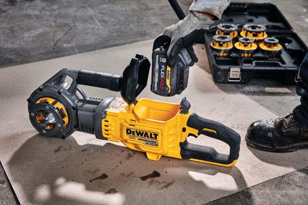 Una herramienta eléctrica sin escobillas DEWALT está mostrada en el suelo, con una persona usando guantes de trabajo insertando una batería FLEXVOLT en la herramienta. En el fondo, hay un estuche con accesorios para la herramienta.