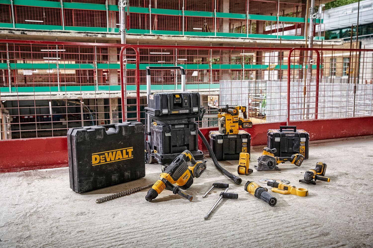 Una colección de herramientas eléctricas y cajas de herramientas DEWALT dispuestas en el suelo de una obra. Las herramientas incluyen taladros, una amoladora y otros equipos, con cajas de herramientas negras y amarillas visibles al fondo.