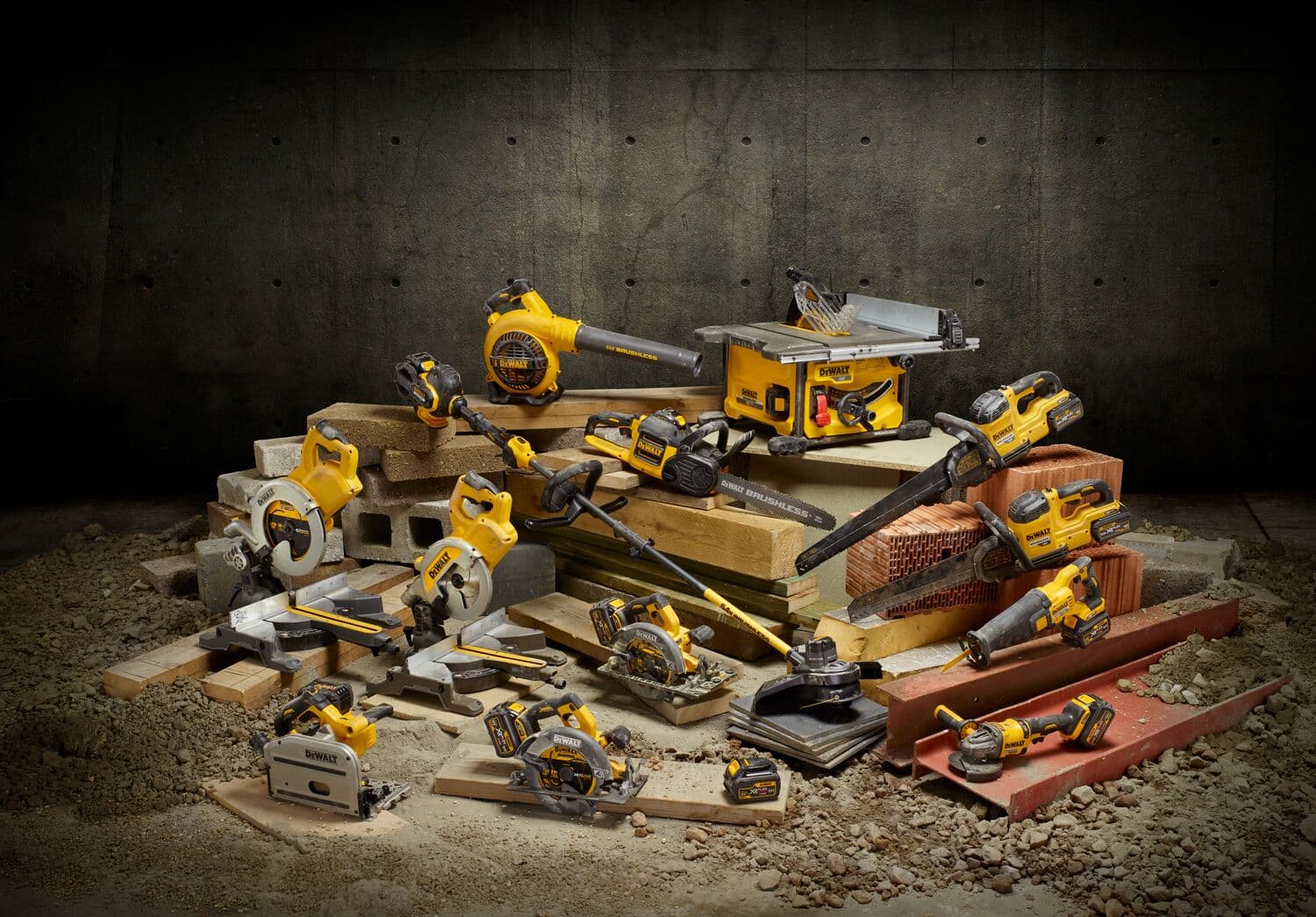 Una colección de herramientas eléctricas DEWALT amarillas y negras se muestra sobre una pila de ladrillos y tablas de madera en un taller. Las herramientas incluyen sierras, taladros, un soplador y otros equipos.