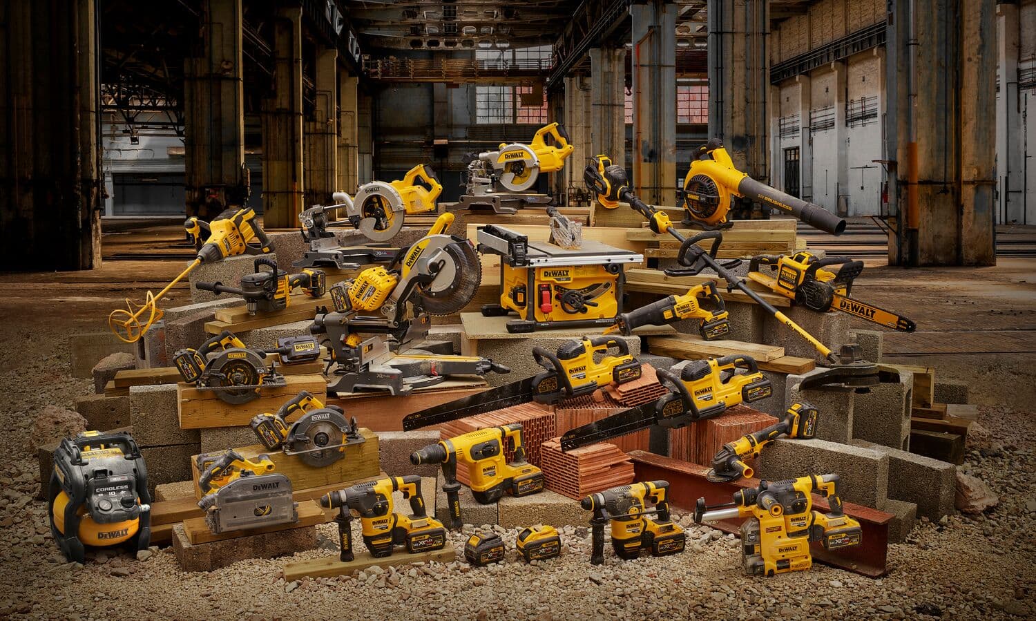 Una variedad de herramientas eléctricas y equipos DEWALT, como sierras, taladros, sopladores, amoladoras y baterías, están dispuestos sobre materiales de construcción como ladrillos y bloques de concreto en un entorno de almacén industrial.