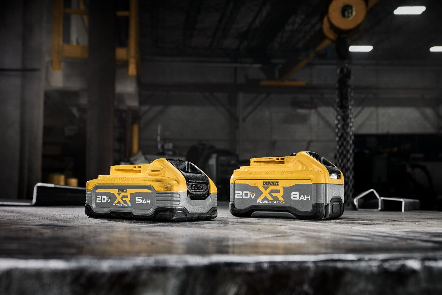 Dos baterías de herramientas eléctricas DEWALT XR de ion de litio, una de 20V 5Ah y otra de 20V 8Ah, se muestran sobre un banco de trabajo en un entorno industrial.